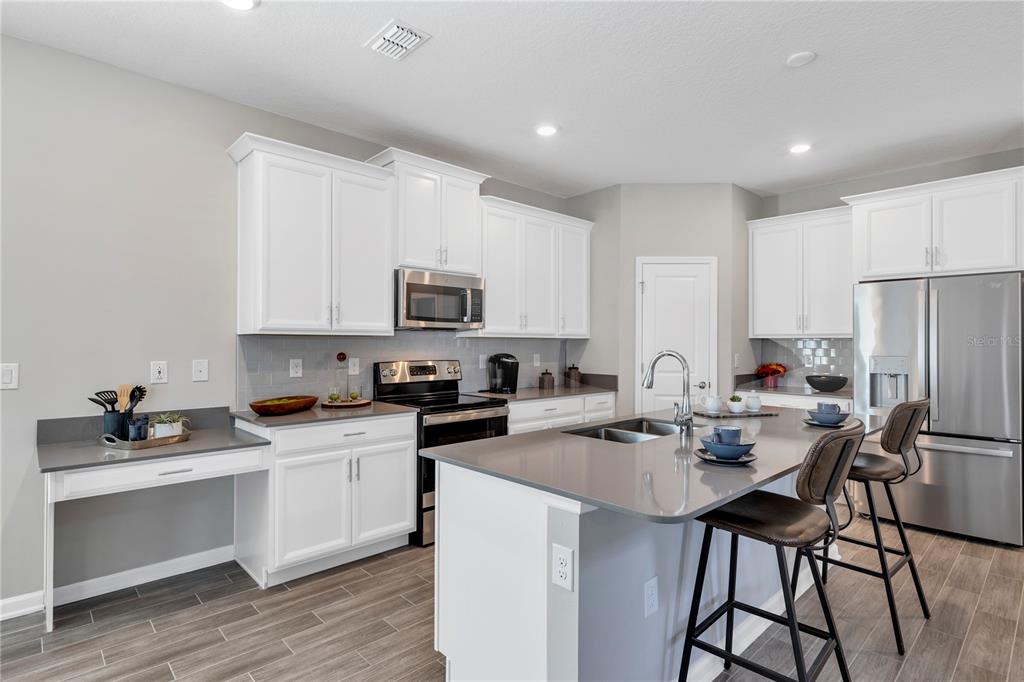 A modern kitchen features white cabinetry, gray countertops, stainless steel appliances, and a central island — 6092 MEDITATION DRIVE, CLERMONT, FL
