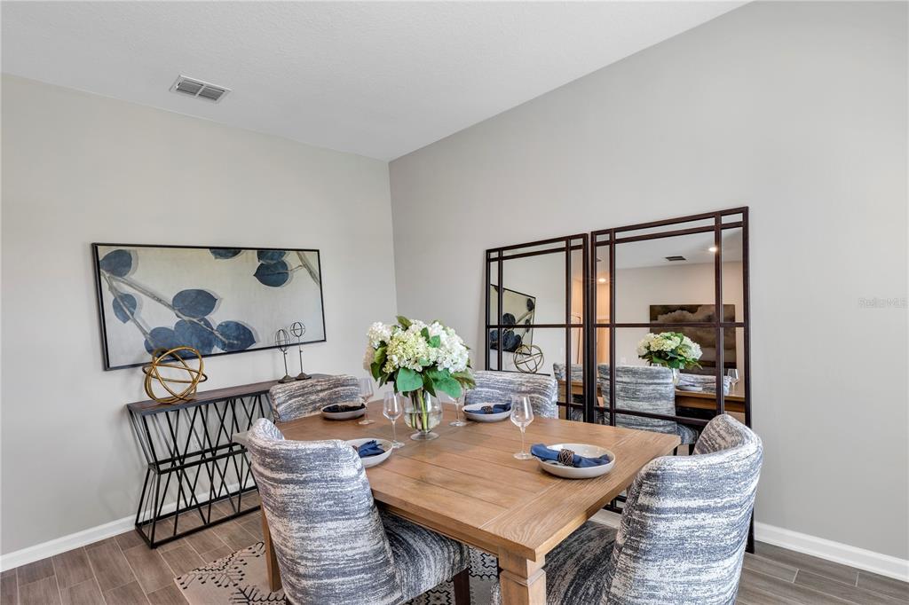 A dining room features a wooden table, upholstered chairs, a console table, and wall mirrors — 6092 MEDITATION DRIVE, CLERMONT, FL