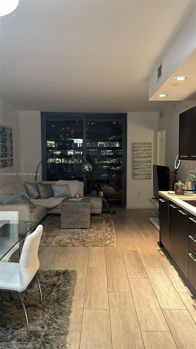 A modern living room and kitchen area features tile flooring, a sectional sofa, and balcony views — 45 SW 9th St # 1409, Miami FL 33130, MIAMI, FL