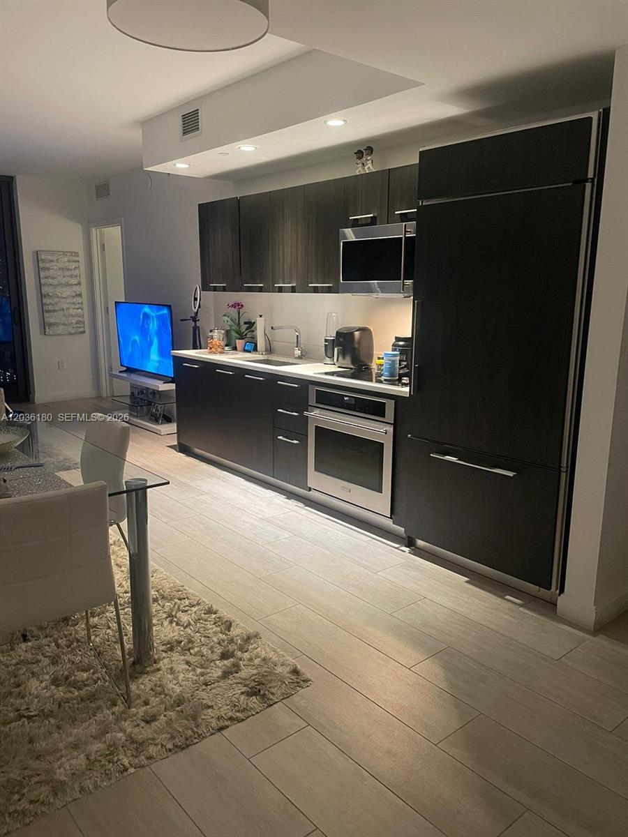 A modern kitchen features dark wood cabinetry, stainless steel appliances, and light tile flooring — 45 SW 9th St # 1409, Miami FL 33130, MIAMI, FL