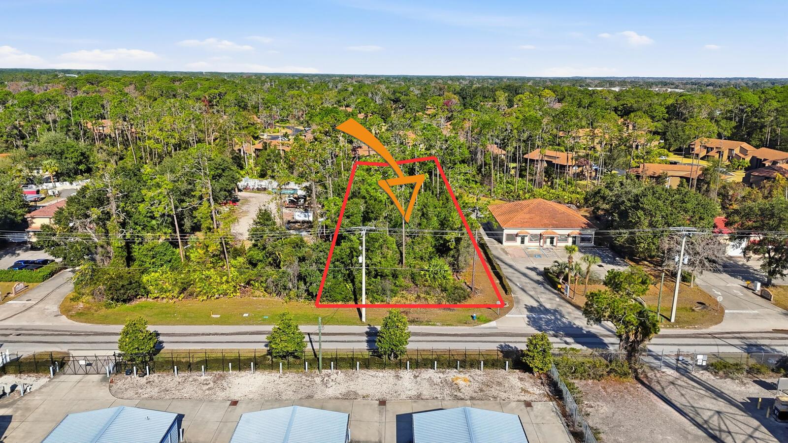 An aerial view shows a vacant, wooded lot outlined in red next to a commercial building — 19 Utility Drive, Palm Coast FL 32137, PALM COAST, FL