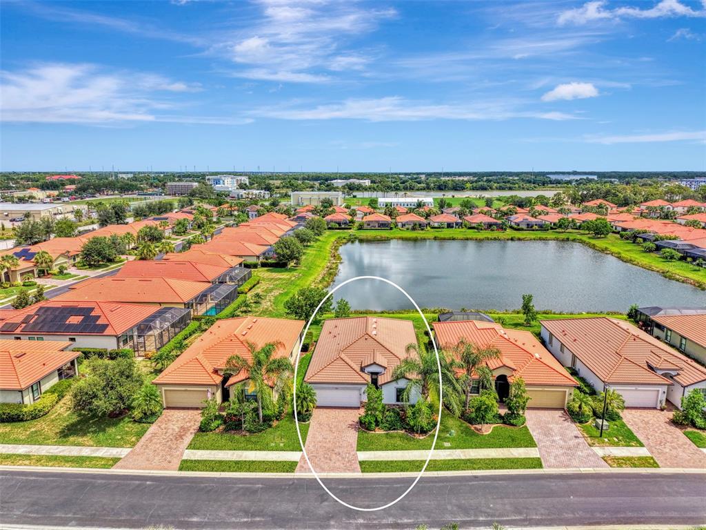 An aerial view shows a single-story house with a tiled roof facing a neighborhood pond — 9824 HILLTOP DRIVE, VENICE, FL
