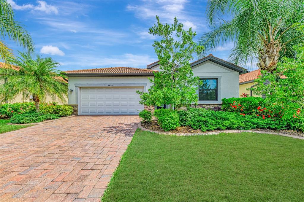 A single-story house with a brick driveway, a two-car garage, and lush landscaping — 9824 HILLTOP DRIVE, VENICE, FL
