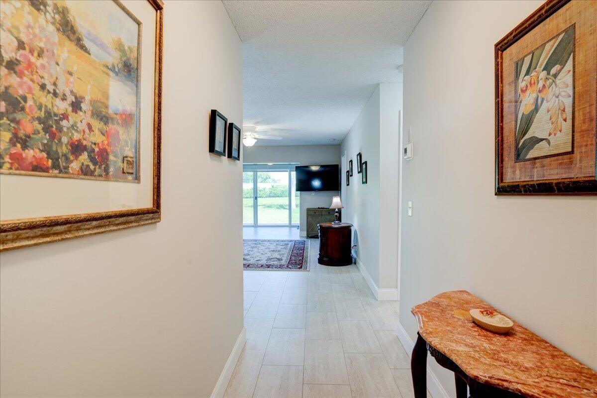 A hallway with tile flooring leads to a living area with a view of greenery — 100 Leisure Lake Circle # 109, Boynton Beach FL 33426, BOYNTON BEACH, FL