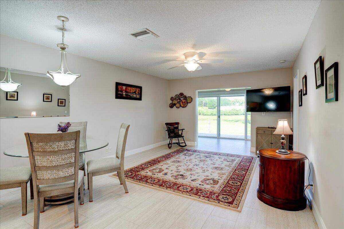 A dining and living area features a glass table, area rug, and sliding glass doors — 100 Leisure Lake Circle # 109, Boynton Beach FL 33426, BOYNTON BEACH, FL