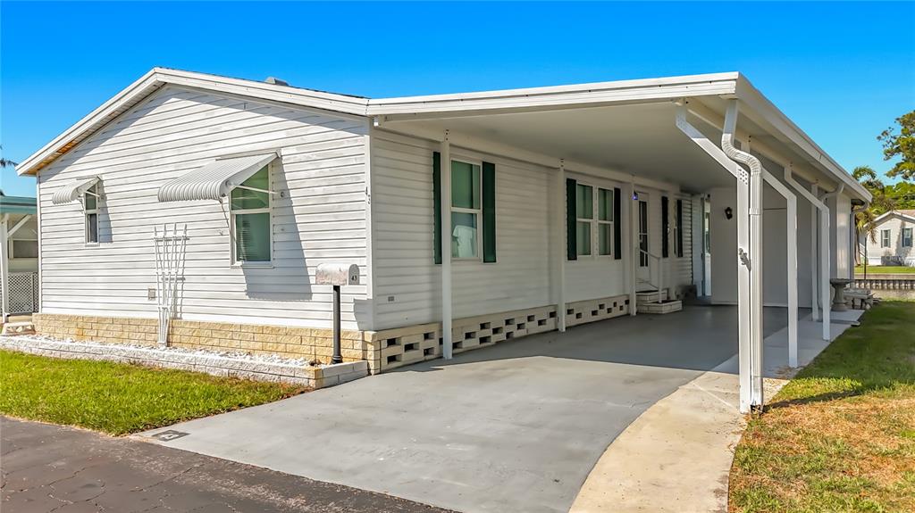 A white mobile home features a carport, a brick-patterned foundation, and a small mailbox — 980 7TH STREET NW UNIT 43, LARGO, FL