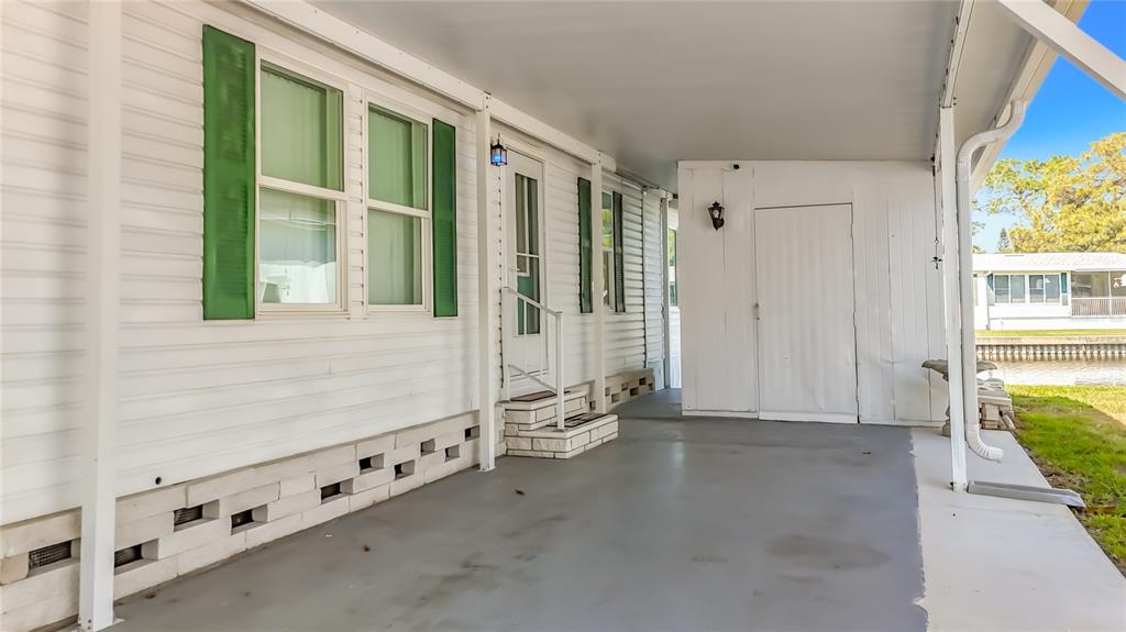 A covered carport area with a white door, siding, and a concrete floor — 980 7TH STREET NW UNIT 43, LARGO, FL