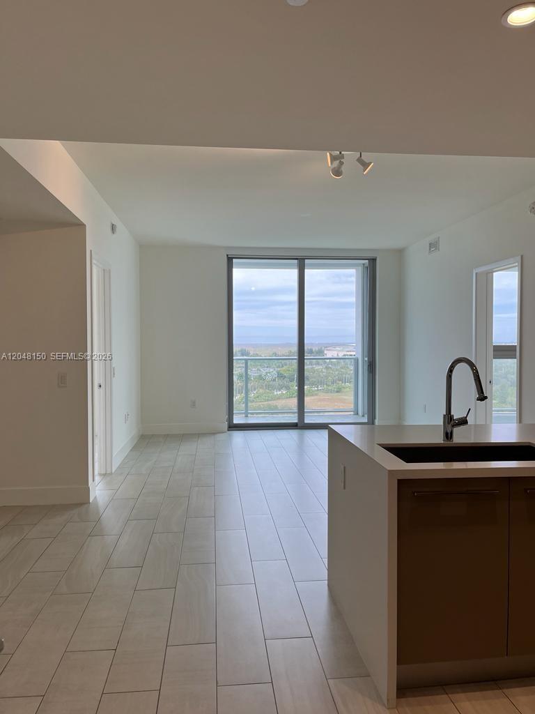 A modern kitchen island overlooks a living area with tile floors and a balcony view — 2000 Metropica Way # 1602, Sunrise FL 33323, SUNRISE, FL