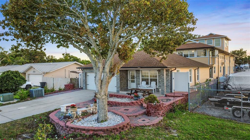 A single-story house with a white garage, stone facade, and a brick patio with landscaping — 5414 RIVERSIDE DRIVE, PORT ORANGE, FL