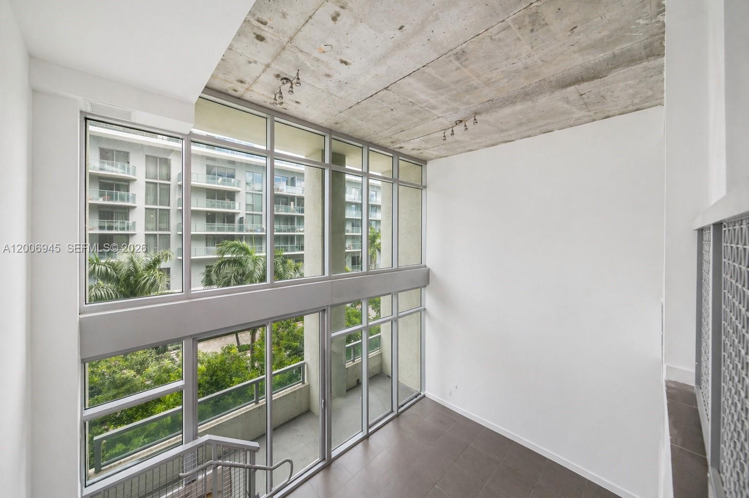A high-ceilinged room features floor-to-ceiling windows, a raw concrete ceiling, and dark tile flooring — 3301 NE 1st Ave # M0308, Miami FL 33137, MIAMI, FL