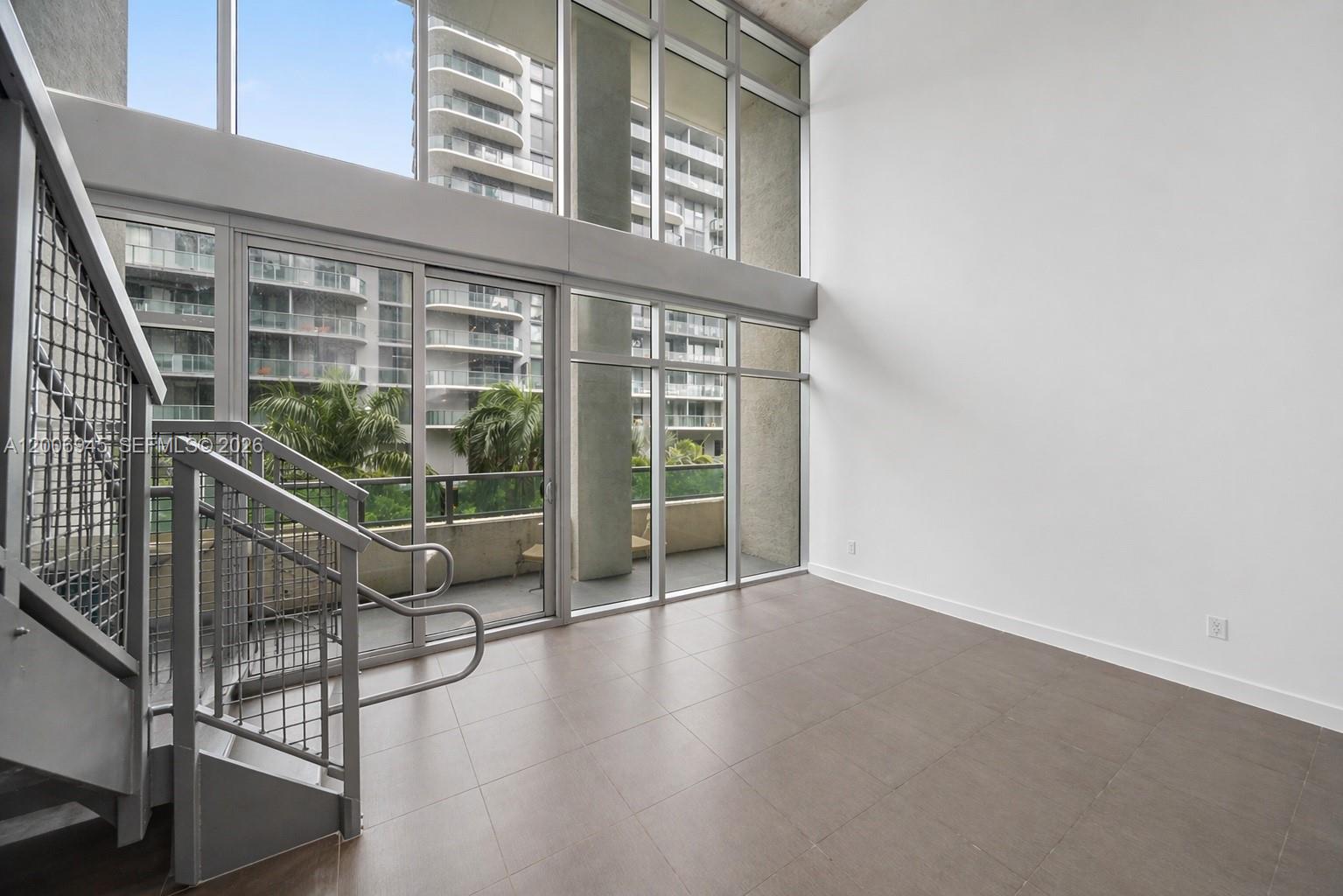 A modern room features double-height windows, a metal staircase, and large gray floor tiles — 3301 NE 1st Ave # M0308, Miami FL 33137, MIAMI, FL