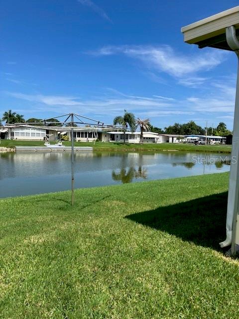 A backyard lawn overlooks a pond with a clothesline and distant houses under a blue sky — 3201 BREWSTER DRIVE, HOLIDAY, FL
