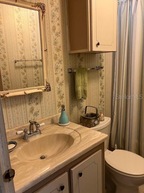 A bathroom features a vanity with a sink, a mirror, wallpaper, and a toilet — 3201 BREWSTER DRIVE, HOLIDAY, FL