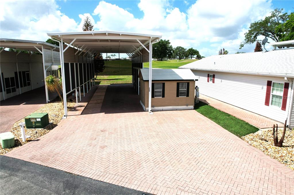 A paved driveway features a large metal carport and a small storage shed between two homes — 1150 DEER CREEK BOULEVARD, DAVENPORT, FL