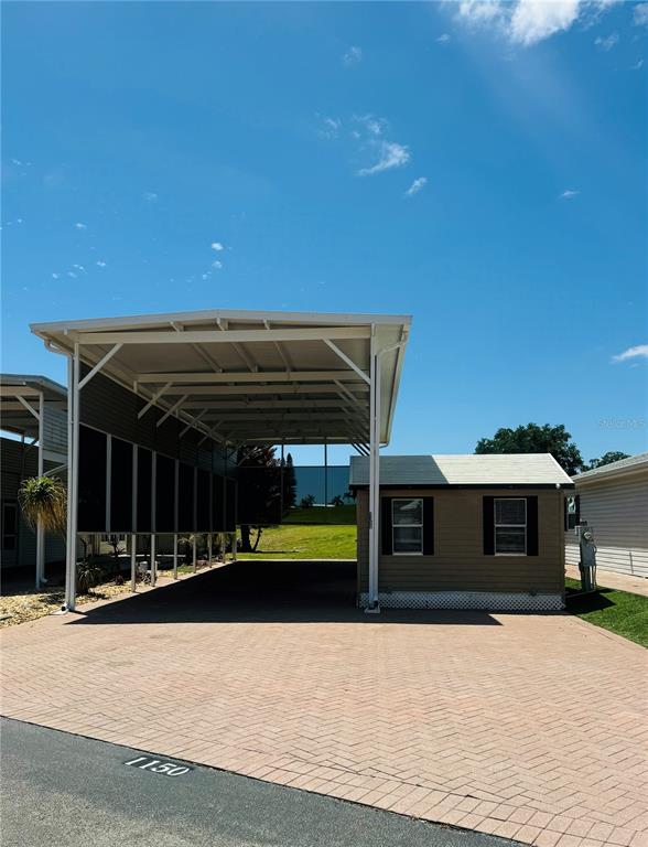 A tan mobile home features a large attached metal carport over a paved driveway — 1150 DEER CREEK BOULEVARD, DAVENPORT, FL