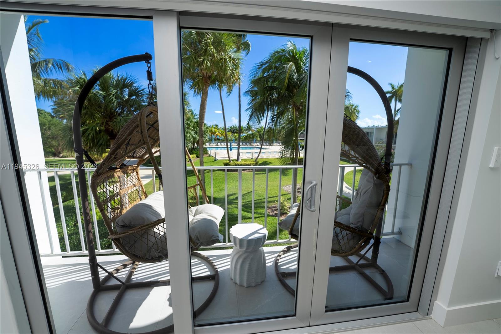 A balcony features two hanging wicker chairs and a small table overlooking a pool area — 881 Ocean Dr, Key Biscayne FL 33149, KEY BISCAYNE, FL