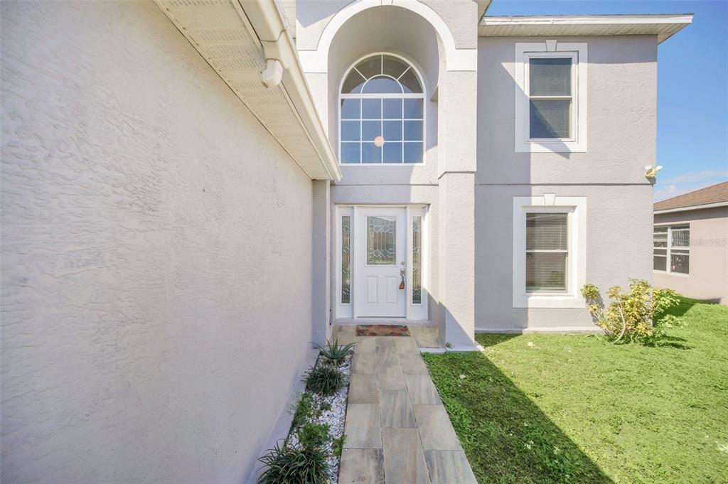 A stone walkway leads to the white front door of a two-story gray stucco house — 2120 MARISOL LOOP, KISSIMMEE, FL