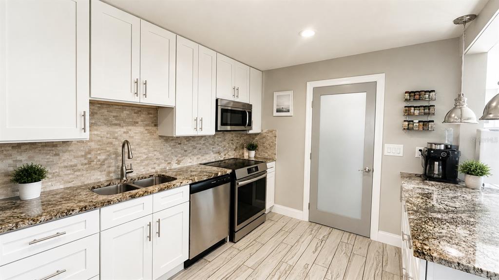 A kitchen features white cabinets, granite countertops, stainless steel appliances, and light wood-look tile flooring — 3606 S RENELLIE DRIVE, TAMPA, FL
