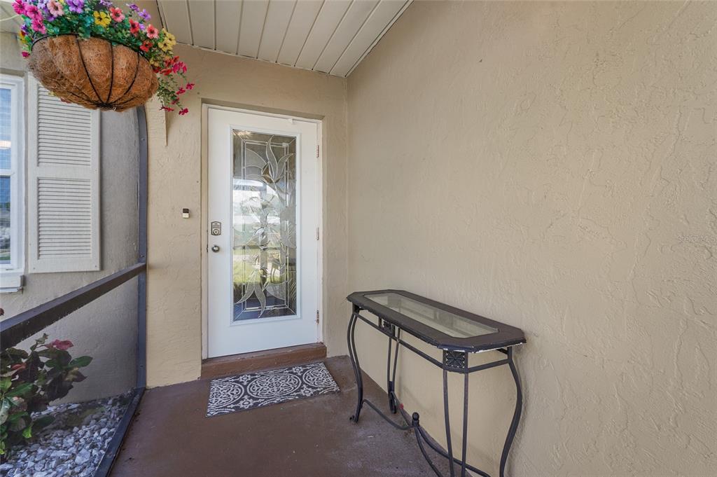 A covered entryway features a white door with decorative glass, a console table, and hanging flowers — 4215 PANDORA ROAD, VENICE, FL