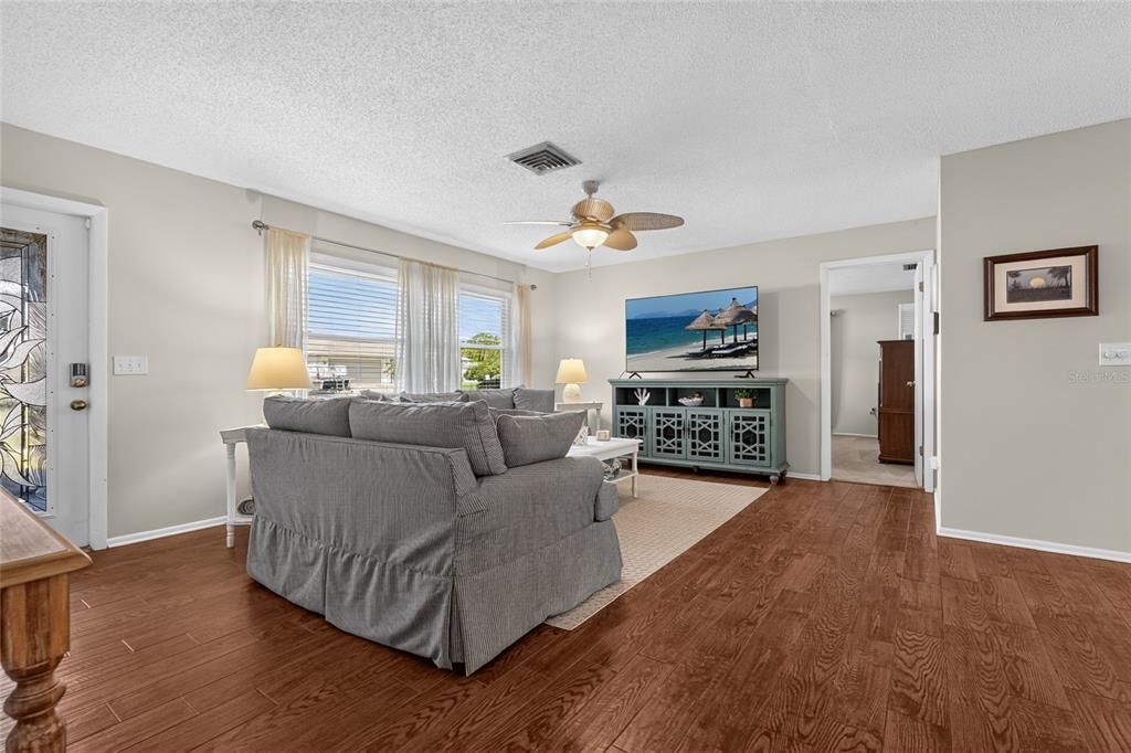 A living room features a gray sofa, a television on a blue console, and wood flooring — 4215 PANDORA ROAD, VENICE, FL