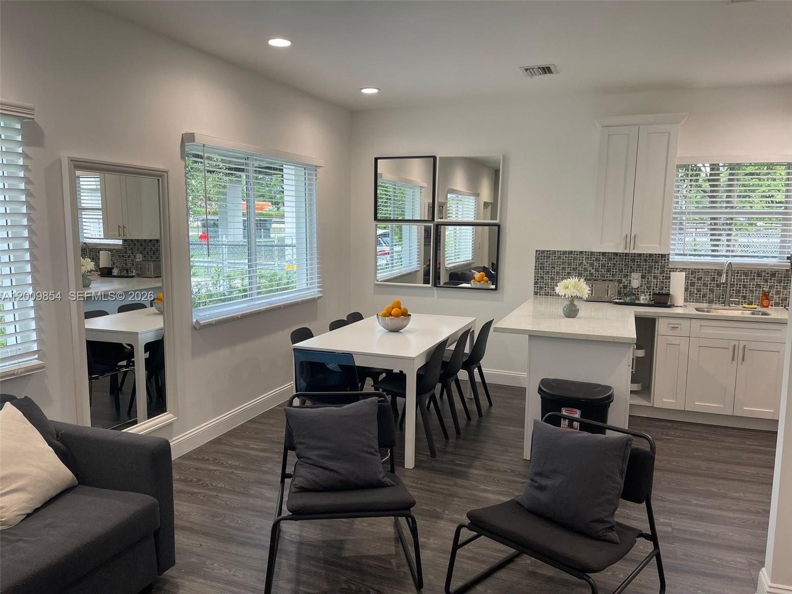 A dining area and kitchen feature white cabinetry, dark wood-look flooring, and modern furniture — 4034 NW 23rd Ave # 0, Miami FL 33142, MIAMI, FL