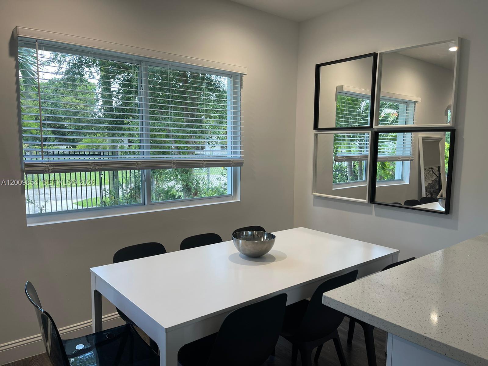 A dining area features a white table, black chairs, a large window, and wall mirrors — 4034 NW 23rd Ave # 0, Miami FL 33142, MIAMI, FL