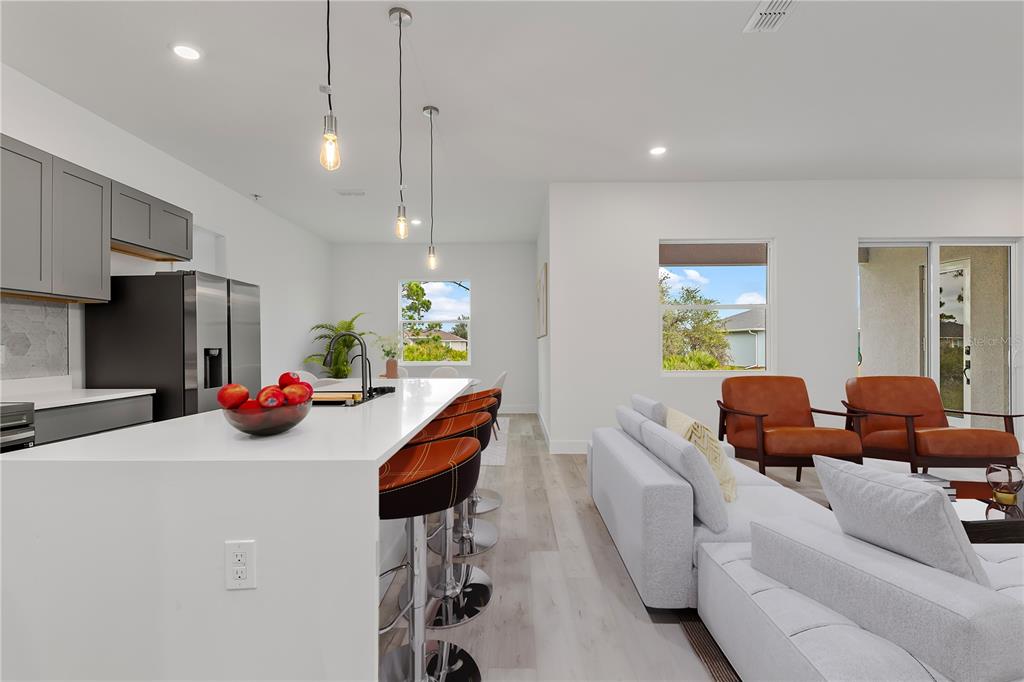 A modern open-concept kitchen and living area featuring white countertops, gray cabinetry, and leather seating — 13514 KEYSTONE BOULEVARD, PORT CHARLOTTE, FL