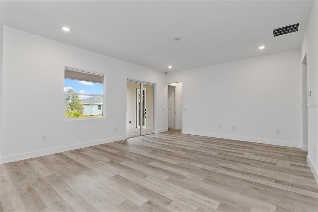 An empty room with light wood-look flooring, white walls, a window, and a sliding glass door — 13514 KEYSTONE BOULEVARD, PORT CHARLOTTE, FL