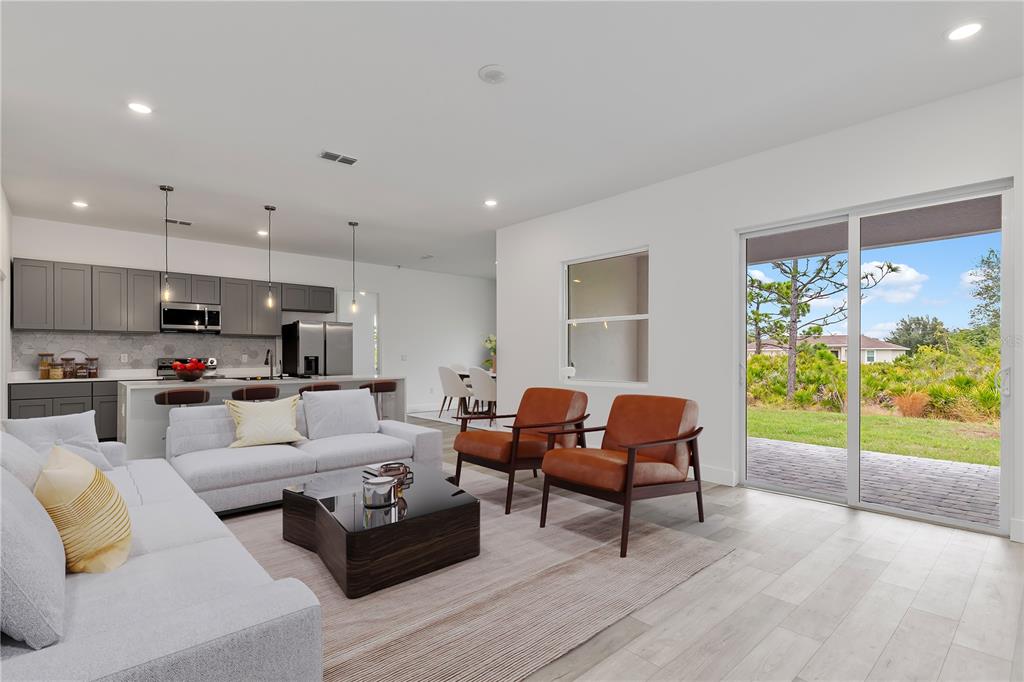 A modern open-concept living room features gray cabinetry, a kitchen island, and sliding glass doors — 13514 KEYSTONE BOULEVARD, PORT CHARLOTTE, FL