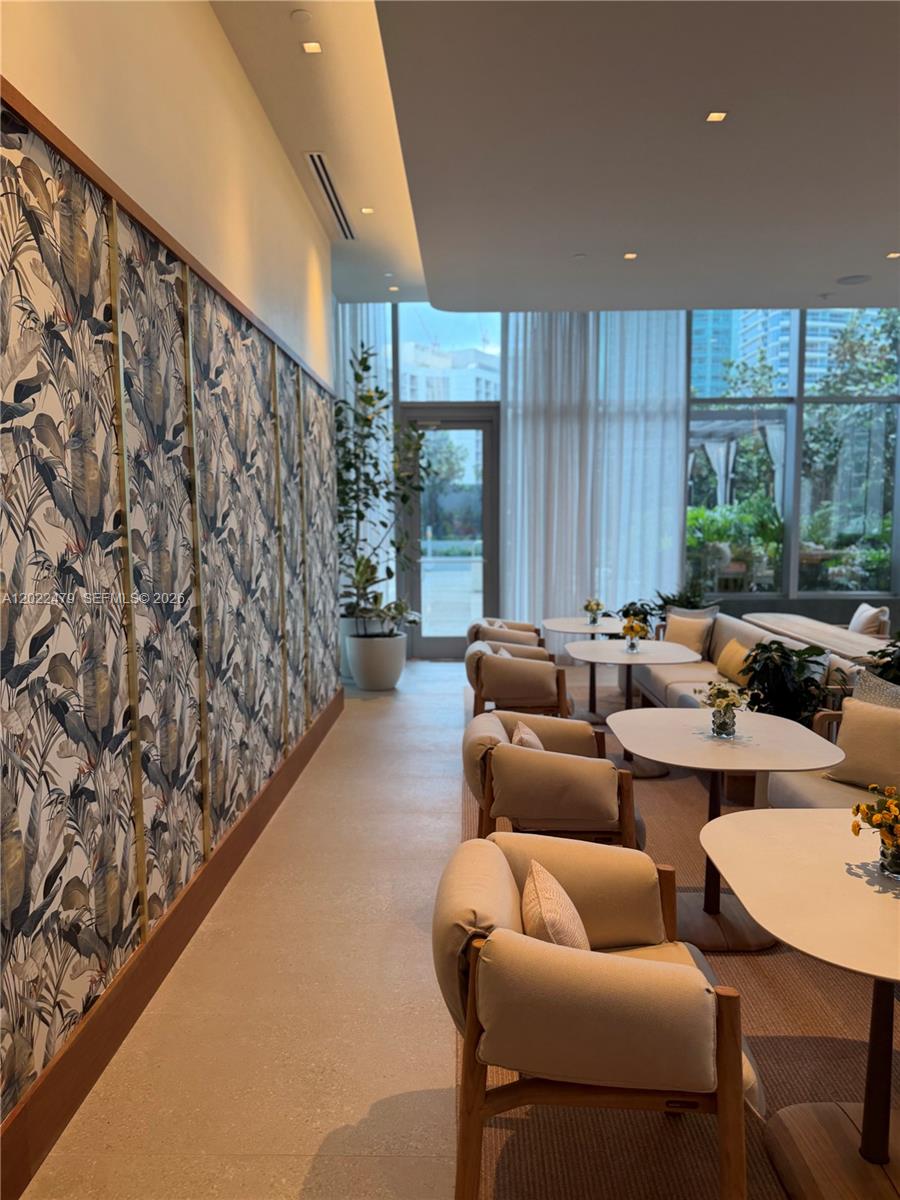 A modern lounge area features patterned wallpaper, light-colored armchairs, and floor-to-ceiling windows — 77 SE 5st # 2306, Miami FL 33131, MIAMI, FL