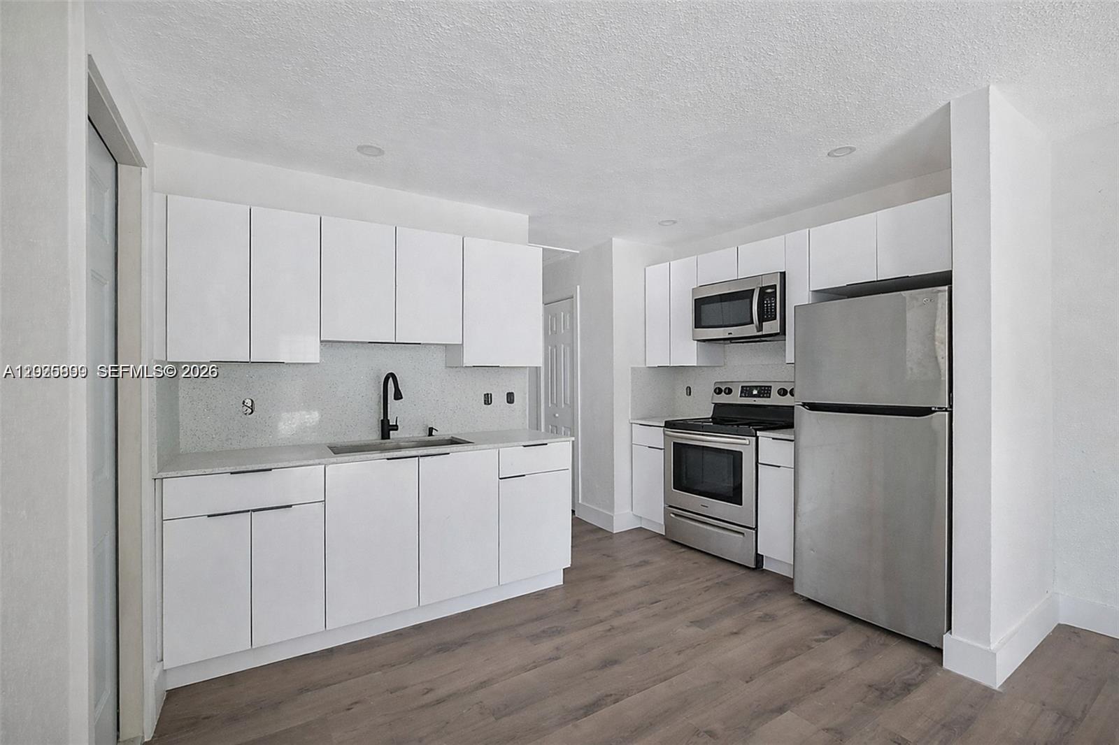 A kitchen features white cabinets, stainless steel appliances, a speckled countertop, and wood-look flooring — 6901 NW 4th Ct # A, Miami FL 33150, MIAMI, FL