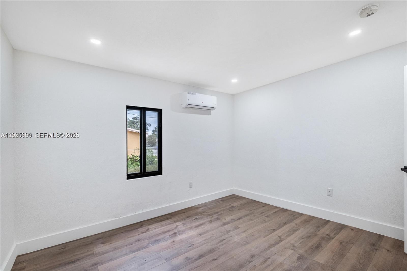 A minimalist room features white walls, wood-look flooring, a small window, and a wall-mounted air conditioner — 6901 NW 4th Ct # A, Miami FL 33150, MIAMI, FL