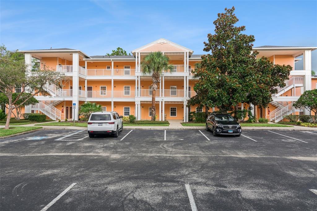 A three-story apartment building with orange siding and white railings sits behind a parking lot — 708 NEW PROVIDENCE PROMENADE, DAVENPORT, FL