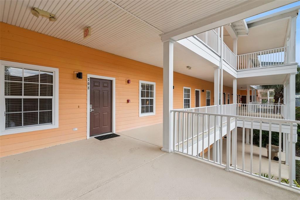 An outdoor covered walkway with orange siding, a brown door, and white railings — 708 NEW PROVIDENCE PROMENADE, DAVENPORT, FL