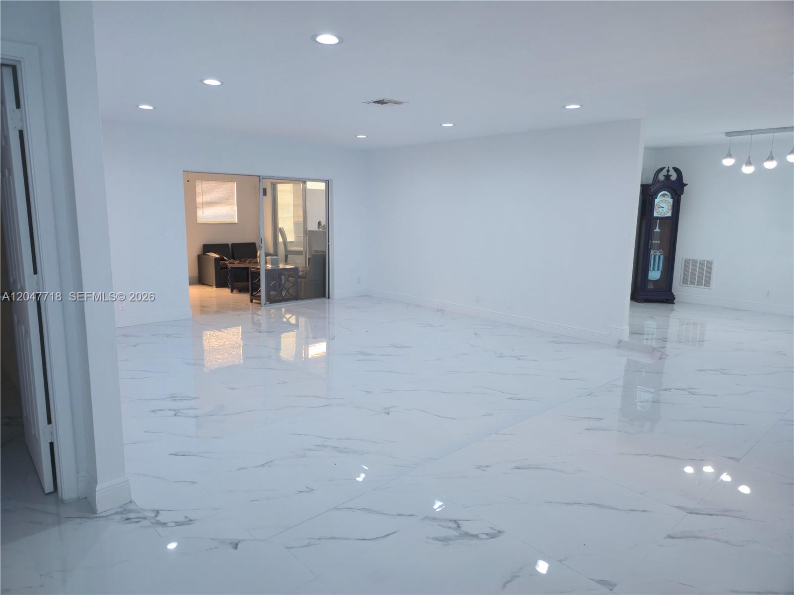 A spacious, empty room features white marble-look tile flooring, recessed lighting, and a sliding glass door — 7771 NW 46th St, Lauderhill FL 33351, LAUDERHILL, FL