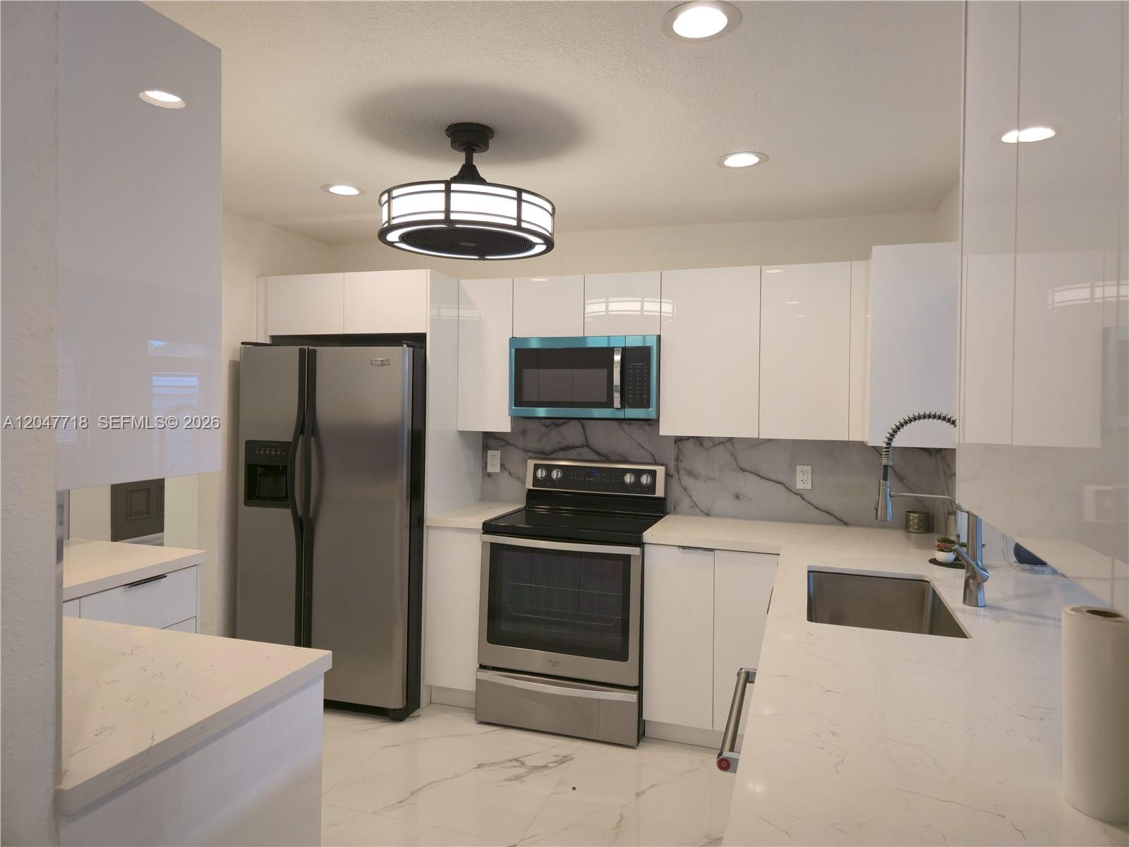 A modern kitchen features white glossy cabinets, stainless steel appliances, and marble-patterned countertops — 7771 NW 46th St, Lauderhill FL 33351, LAUDERHILL, FL