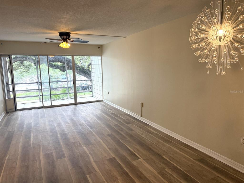 An empty living room features wood-look flooring, a ceiling fan, and a sliding glass door — 2302 S MANHATTAN AVENUE UNIT 219, TAMPA, FL
