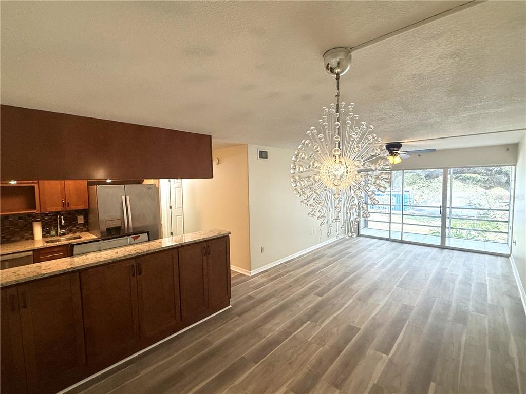 A kitchen with wood cabinets and granite countertops opens into a living area with flooring — 2302 S MANHATTAN AVENUE UNIT 219, TAMPA, FL