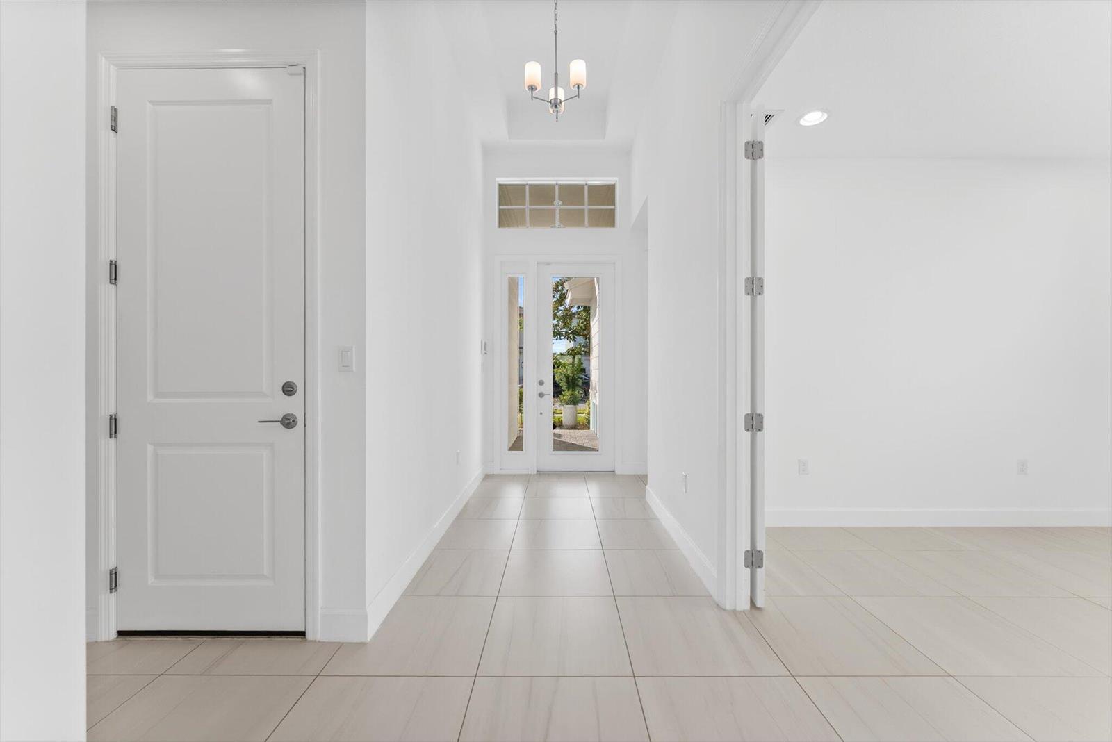 A bright entryway features white walls, tile flooring, a chandelier, and a glass-paneled front door — 1346 Harvester Crossing, Loxahatchee FL 33470, LOXAHATCHEE, FL