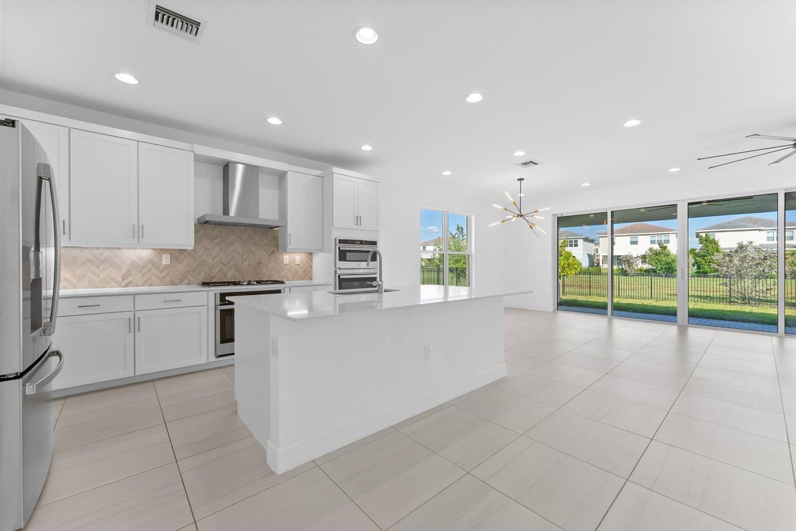 A modern white kitchen features a center island, stainless steel appliances, and large sliding doors — 1346 Harvester Crossing, Loxahatchee FL 33470, LOXAHATCHEE, FL