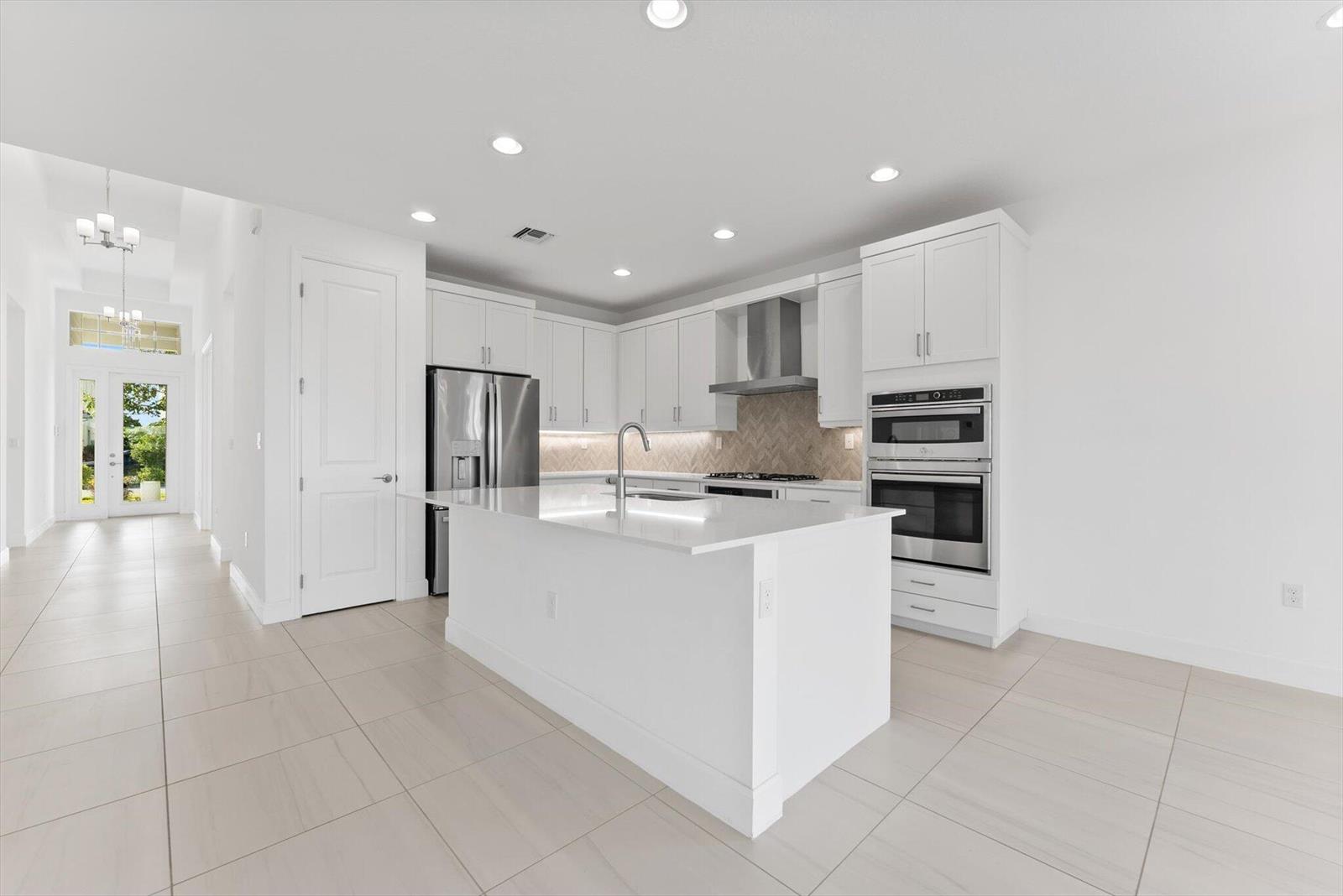 A modern kitchen features white cabinetry, a central island, stainless steel appliances, and tile flooring — 1346 Harvester Crossing, Loxahatchee FL 33470, LOXAHATCHEE, FL
