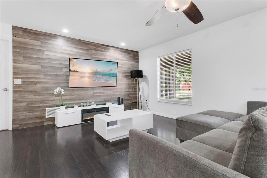 A living room features a wood-paneled accent wall, a wall-mounted television, and dark hardwood floors — 8644 SANDBERRY BOULEVARD, ORLANDO, FL
