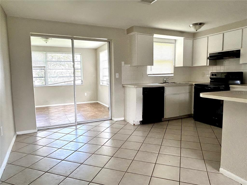 A kitchen with white cabinets, black appliances, and tile flooring opens to a sunroom — 4653 DARLINGTON ROAD, HOLIDAY, FL