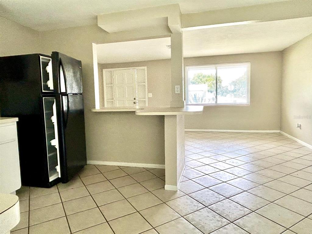 A kitchen with a black refrigerator and a breakfast bar overlooking a tiled living area — 4653 DARLINGTON ROAD, HOLIDAY, FL