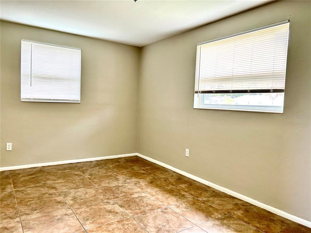 An empty room features tan walls, tile flooring, and two windows with white blinds — 4653 DARLINGTON ROAD, HOLIDAY, FL