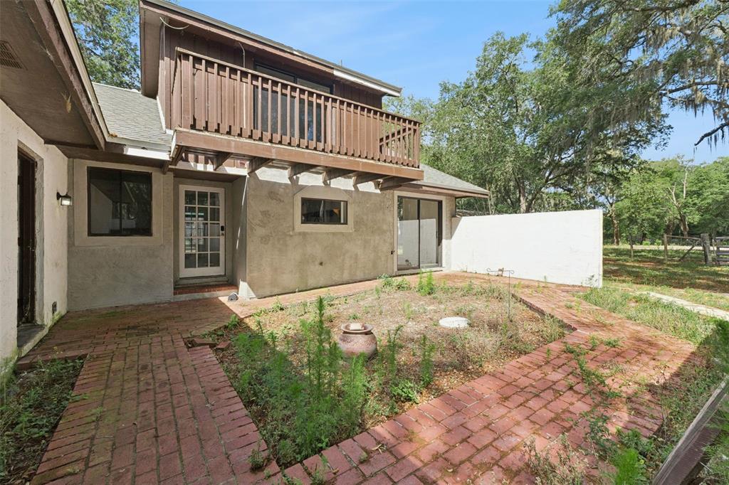 A two-story house exterior features a brick patio, a wooden balcony, and a white wall — 1142 BUCKLES ROAD, PIERSON, FL