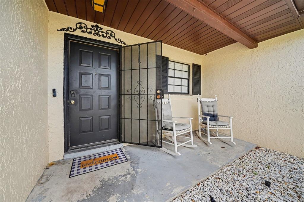 A covered front porch features a black door, a security screen, and two rocking chairs — 1180 BALFOUR DRIVE, DELTONA, FL