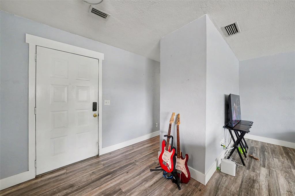 A room with light gray walls, wood-look flooring, a white door, and two electric guitars — 1180 BALFOUR DRIVE, DELTONA, FL