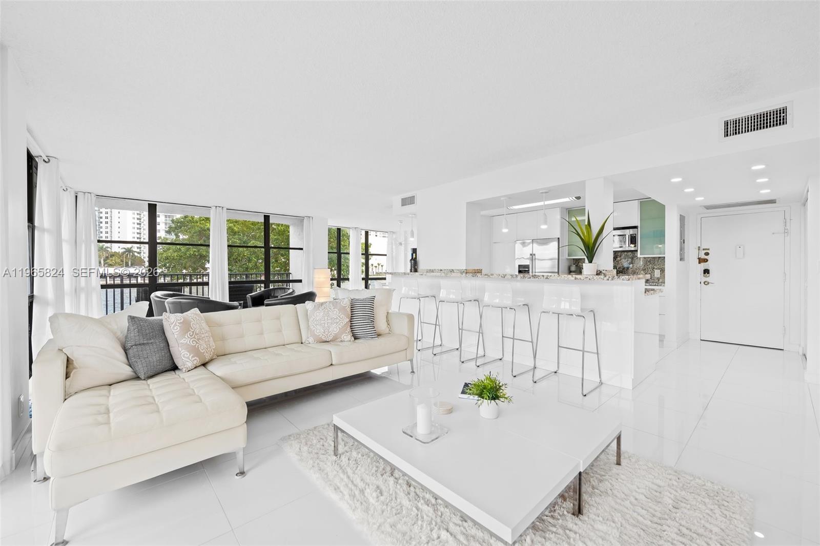 A bright living room features a white sectional sofa, a coffee table, and a kitchen — 800 Parkview Dr # 221, Hallandale Beach FL 33009, HALLANDALE BEACH, FL