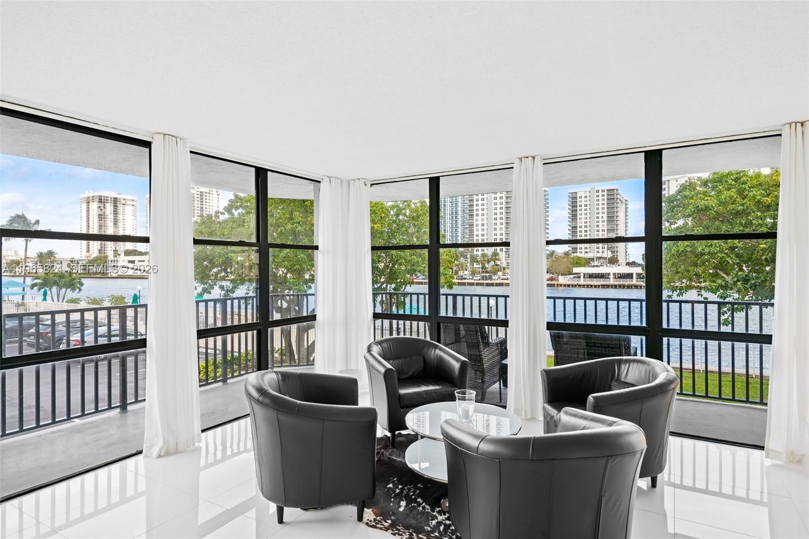 A bright living area features floor-to-ceiling windows, white tile floors, and four black leather chairs — 800 Parkview Dr # 221, Hallandale Beach FL 33009, HALLANDALE BEACH, FL
